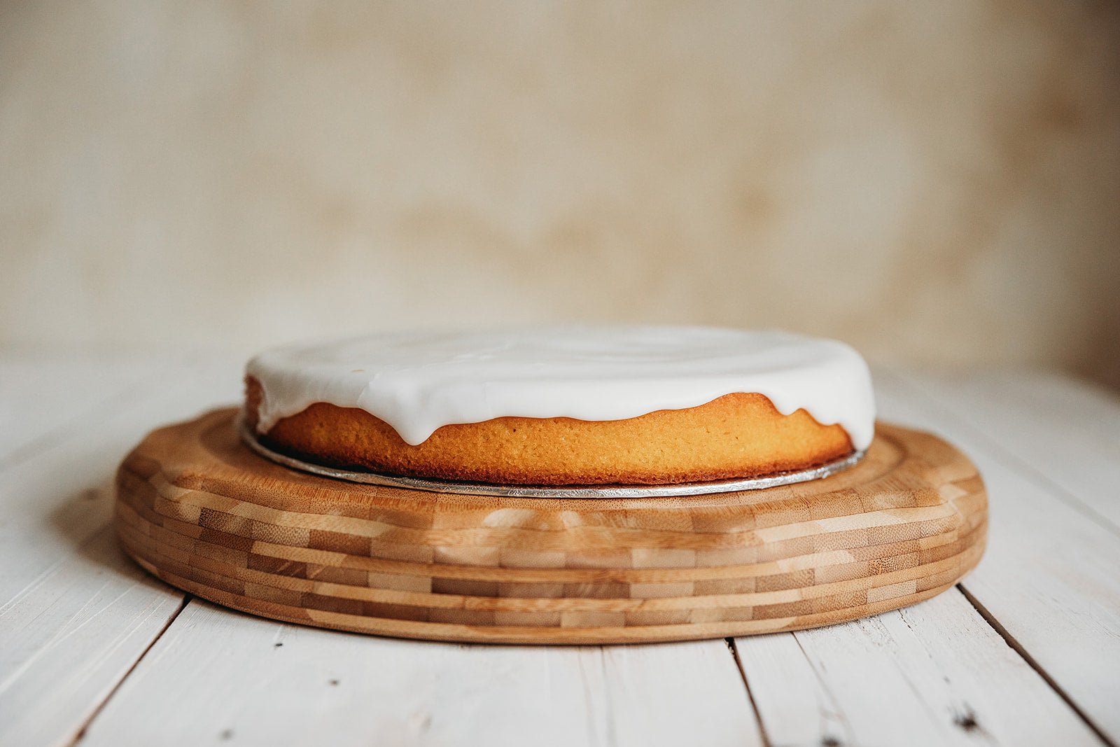 A frosted orange and polenta cake on a wooden round board, with a beige background.