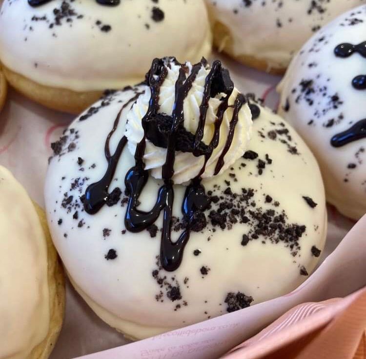 Donut with white icing, chocolate drizzle, and cookie crumb toppings on a pink surface.