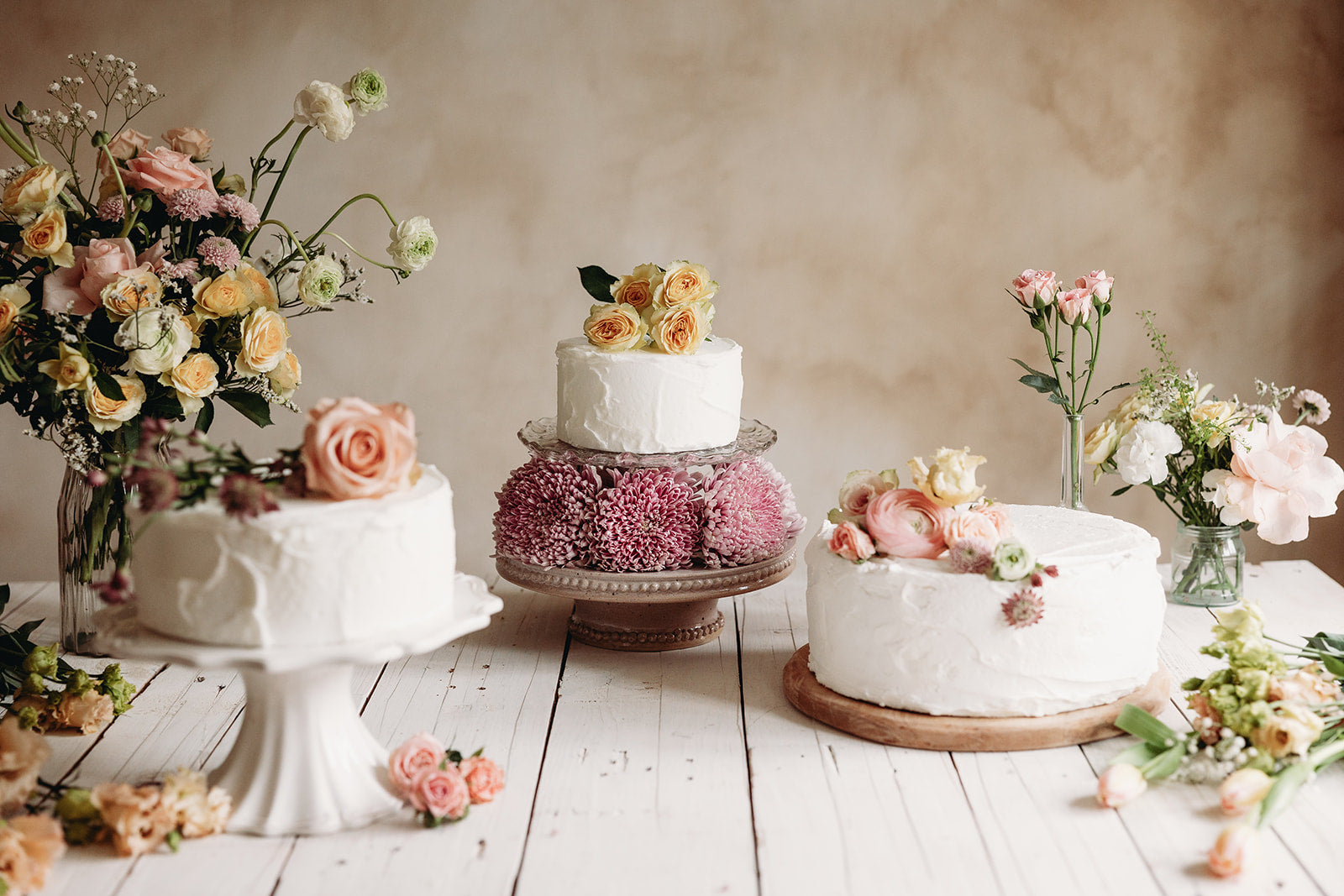 Three wedding cakes on a wooden table with floral decorations