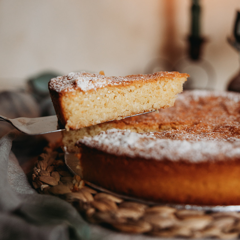 Slice of cake being lifted from a round cake on a woven mat.