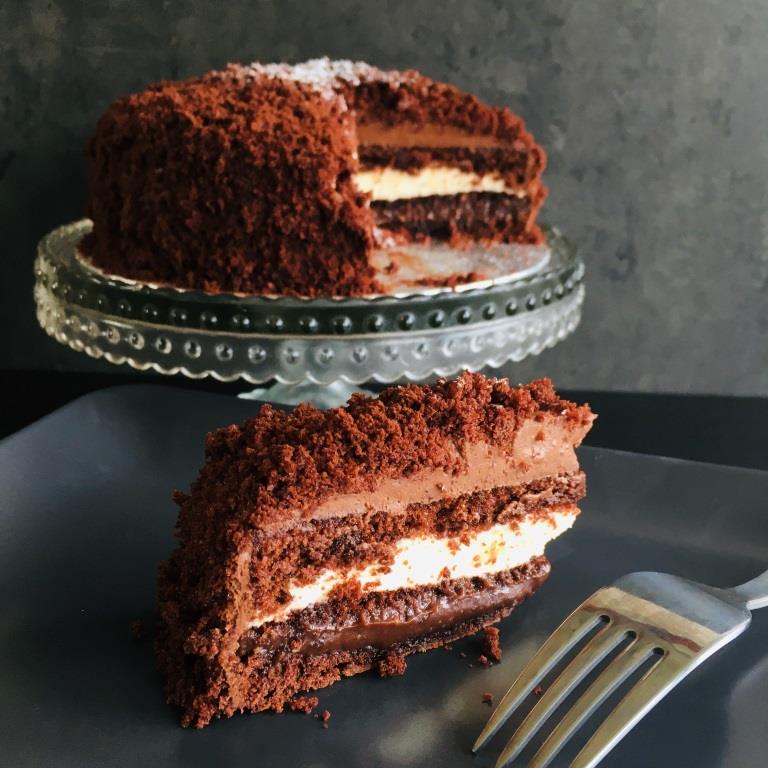 A slice of Chocolate Mimosa cake, served on a plate with a fork, against a grey background. Made by Cambridge based bakery Biscotti di Debora.