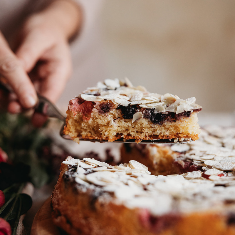 Slice of fresh berry cake being lifted with a spatula, blurred background