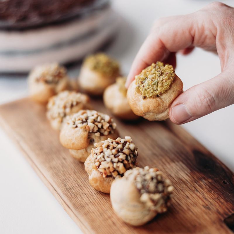 Stuffed petit fours on a wooden board with a hand picking one up.