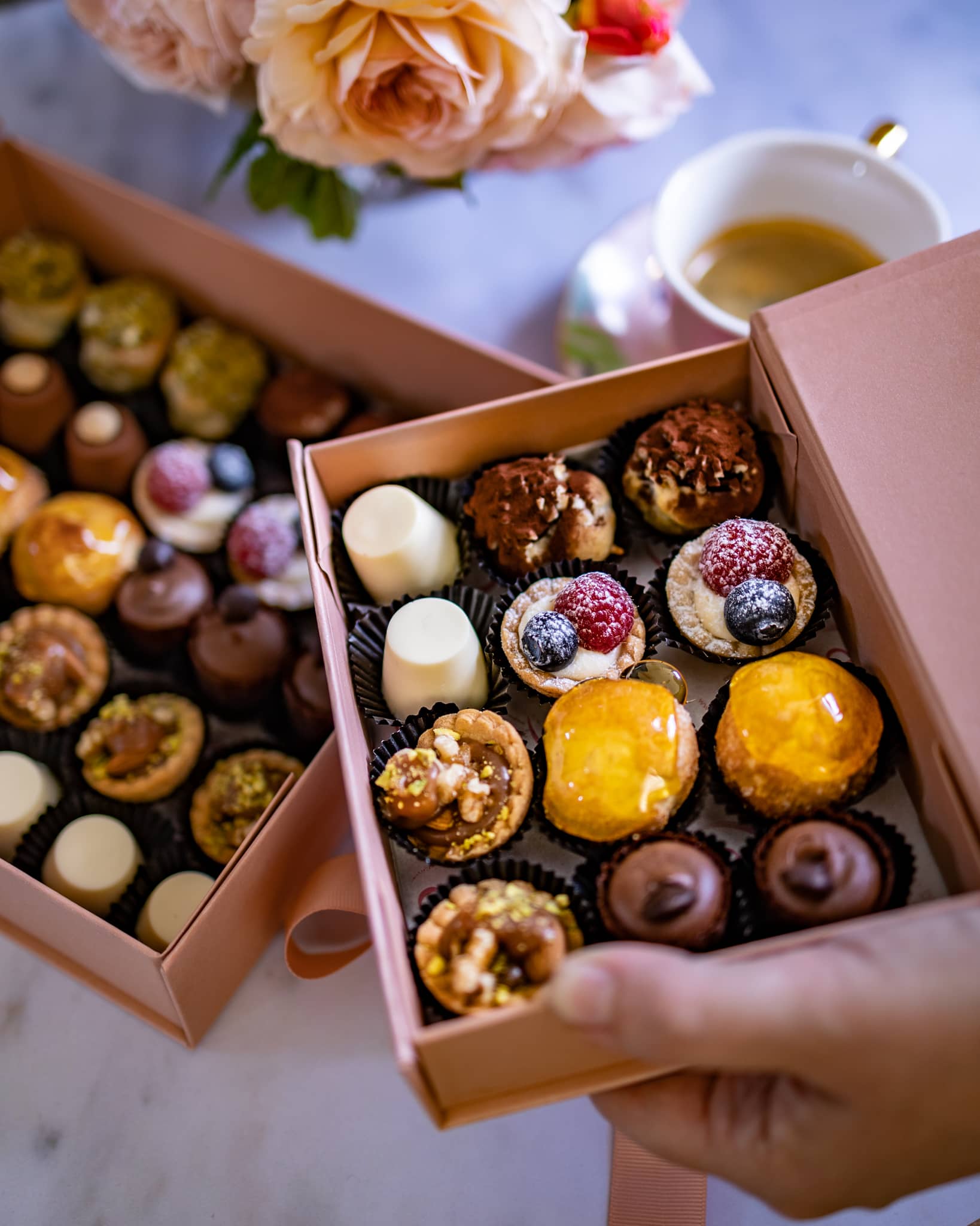 An assortment of petite desserts in a box, featuring pastries with cream, fruit tarts, an assortment of mini desserts, like pannacottas, choux buns filled with crème patisserie, mini meringues sandwiched with cream, shortcrust tartlets with strawberries. Handmade in Cambridge by Biscotti di Debora.