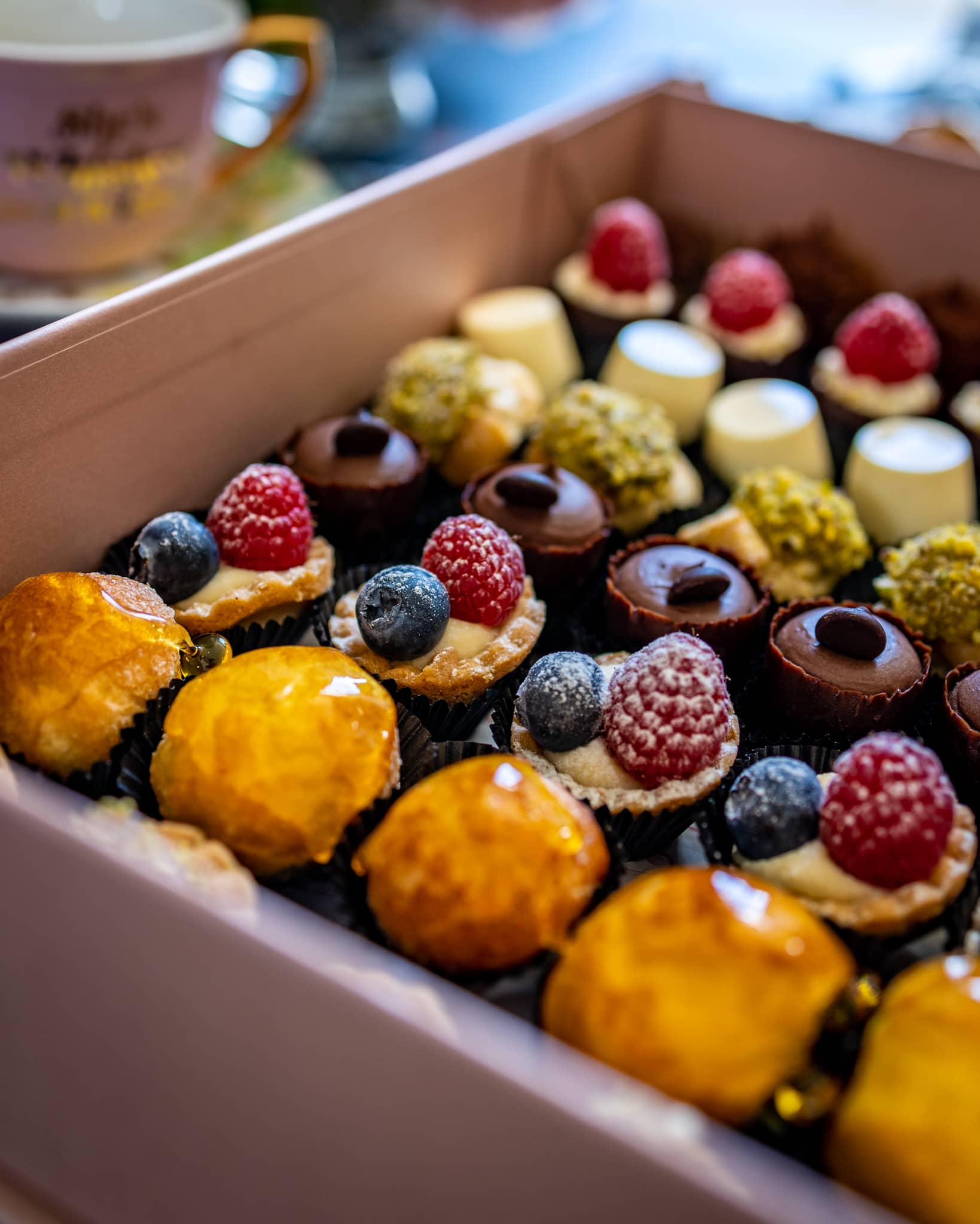 An assortment of petite desserts in a box, featuring assortment of mini desserts, like pannacottas, choux buns filled with crème patisserie, mini meringues sandwiched with cream, shortcrust tartlets with strawberries. Handmade in Cambridge by Biscotti di Debora.