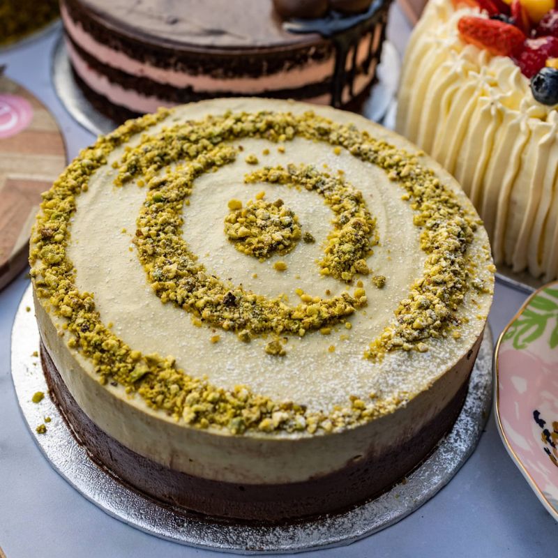 Close-up of a cake with a spiral pistachio decoration on a light blue surface.