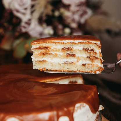 Slice of layered Salted caramel cake on a spatula with blurred floral background