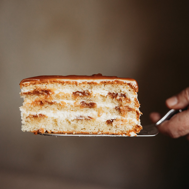 Slice of layered salted caramel cake on a spatula with a blurred background